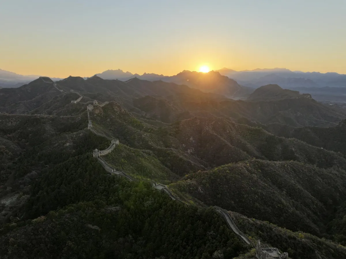 Breathtaking sunrise view of the Great Wall of China winding through lush mountains.