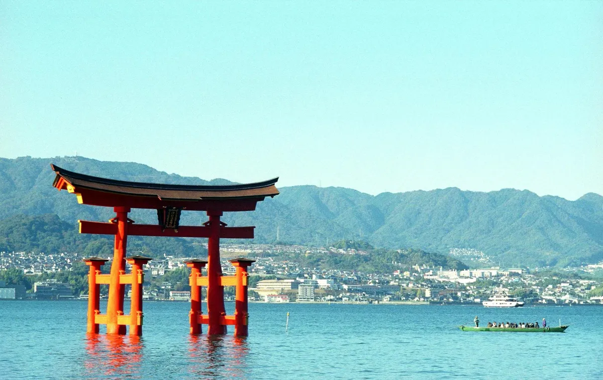 The vibrant red torii gate of Itsukushima Shrine stands elegantly in the sea, framed by mountains.