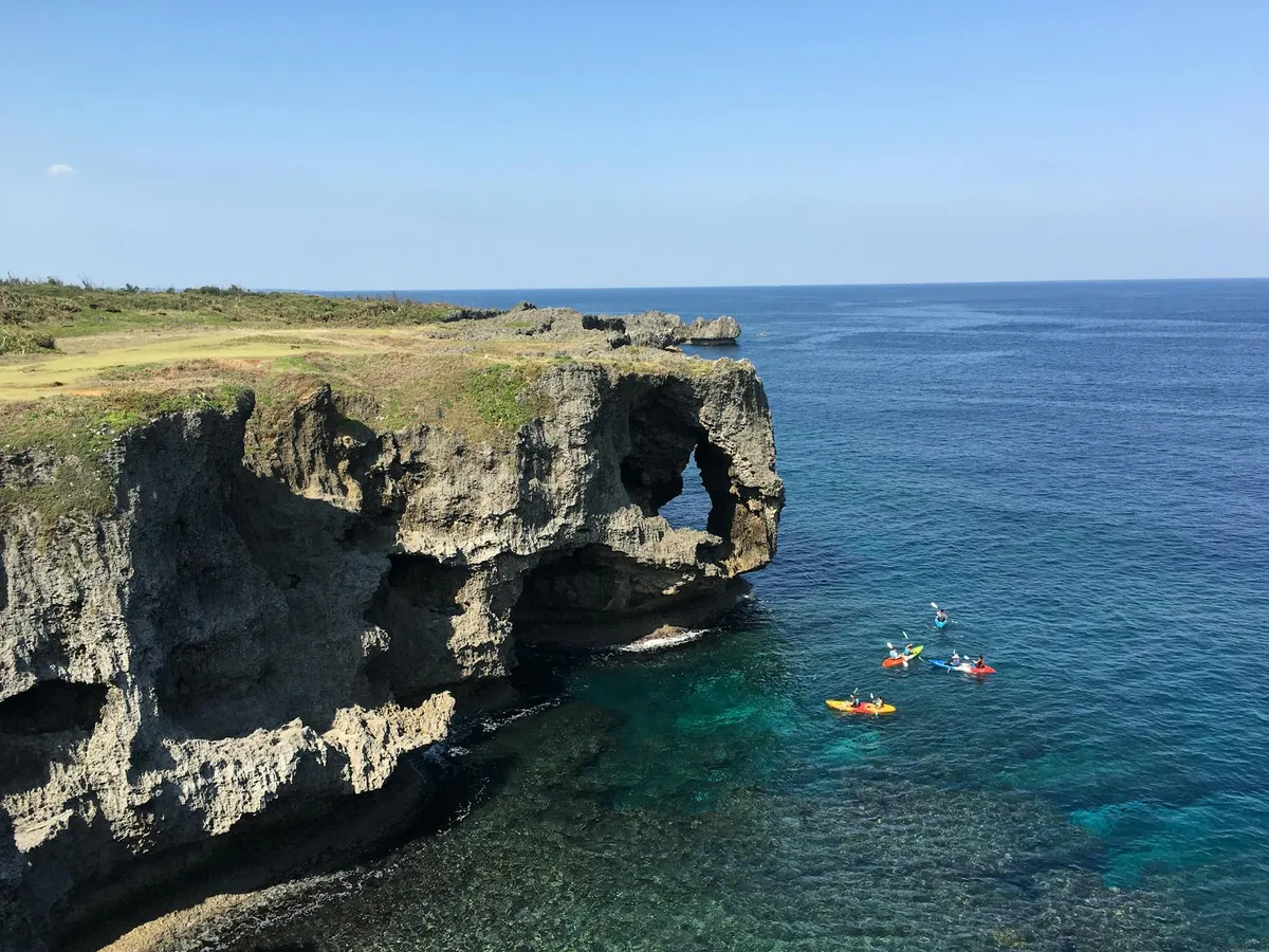 Explore the stunning Cape Manzamo cliffs and clear blue ocean waters in Okinawa, Japan, with kayakers in view.