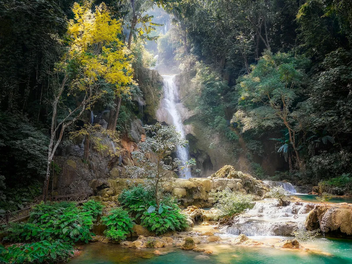 Serene waterfall cascading through dense jungle in Laos, surrounded by vibrant foliage.