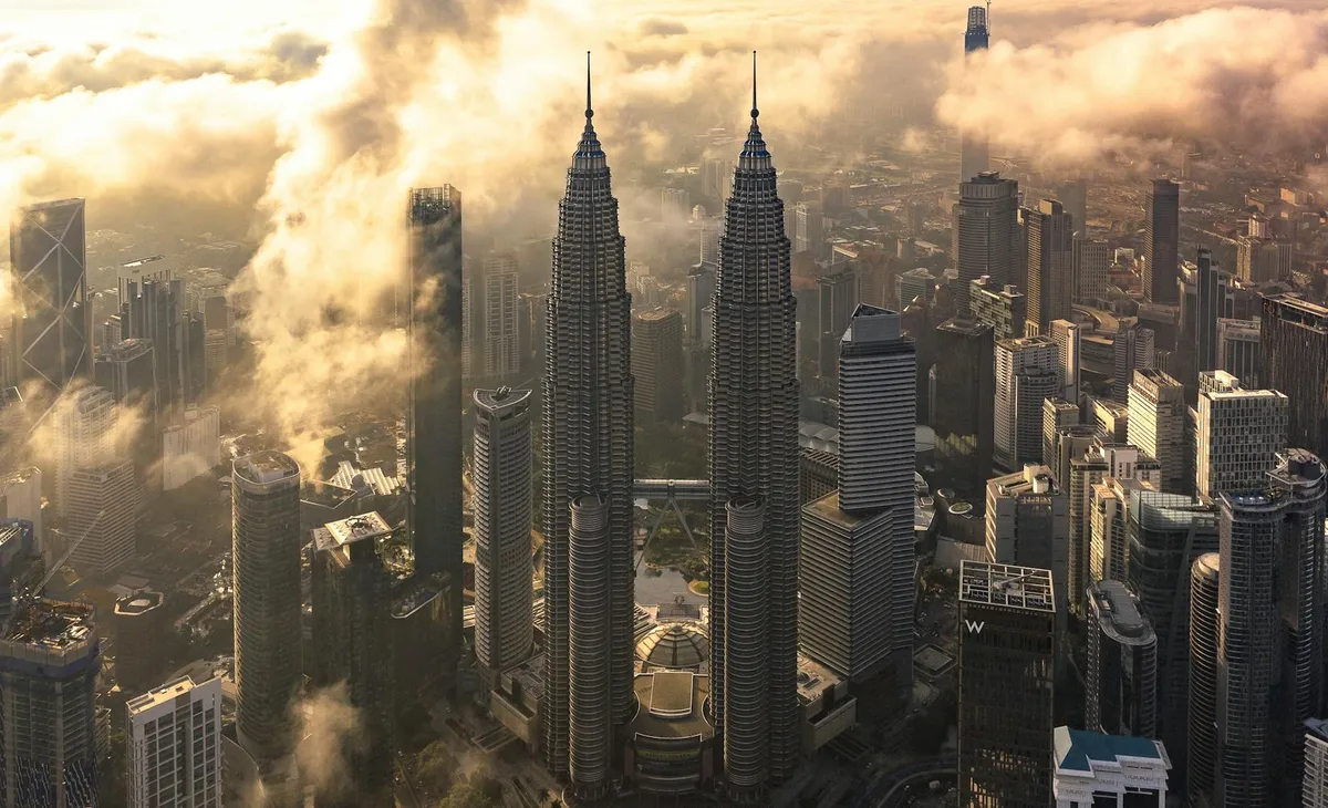 Aerial view of Kuala Lumpur skyline featuring the iconic Petronas Towers at sunset.