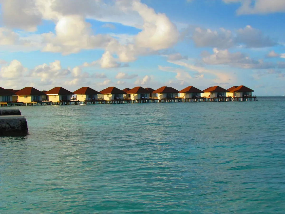 Scenic view of overwater bungalows in Maldives during sunset, showcasing turquoise waters and beautiful skies.