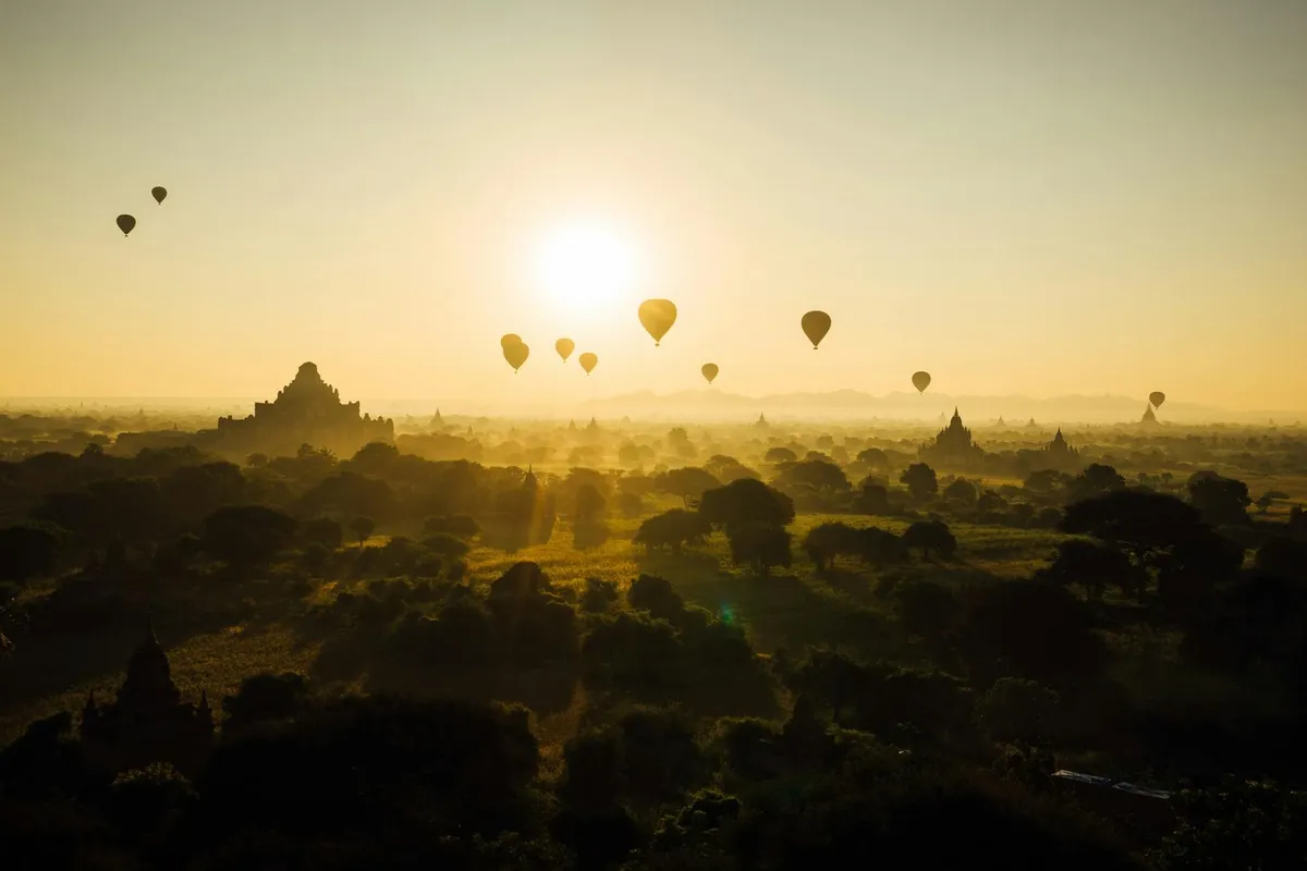 Hot air balloons floating over Bagan temples at sunrise, creating a stunning silhouette against the golden sky.