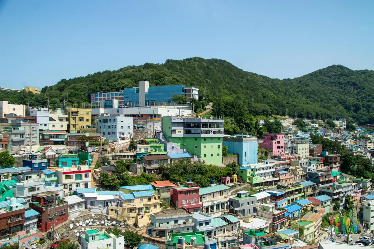 A vibrant aerial view of Busan's Gamcheon Culture Village with colorful houses and lush hills.
