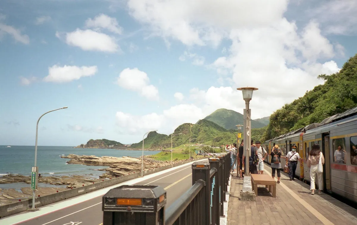 Peaceful view of a coastal railway station in Taipei, Taiwan, with mountains and ocean.
