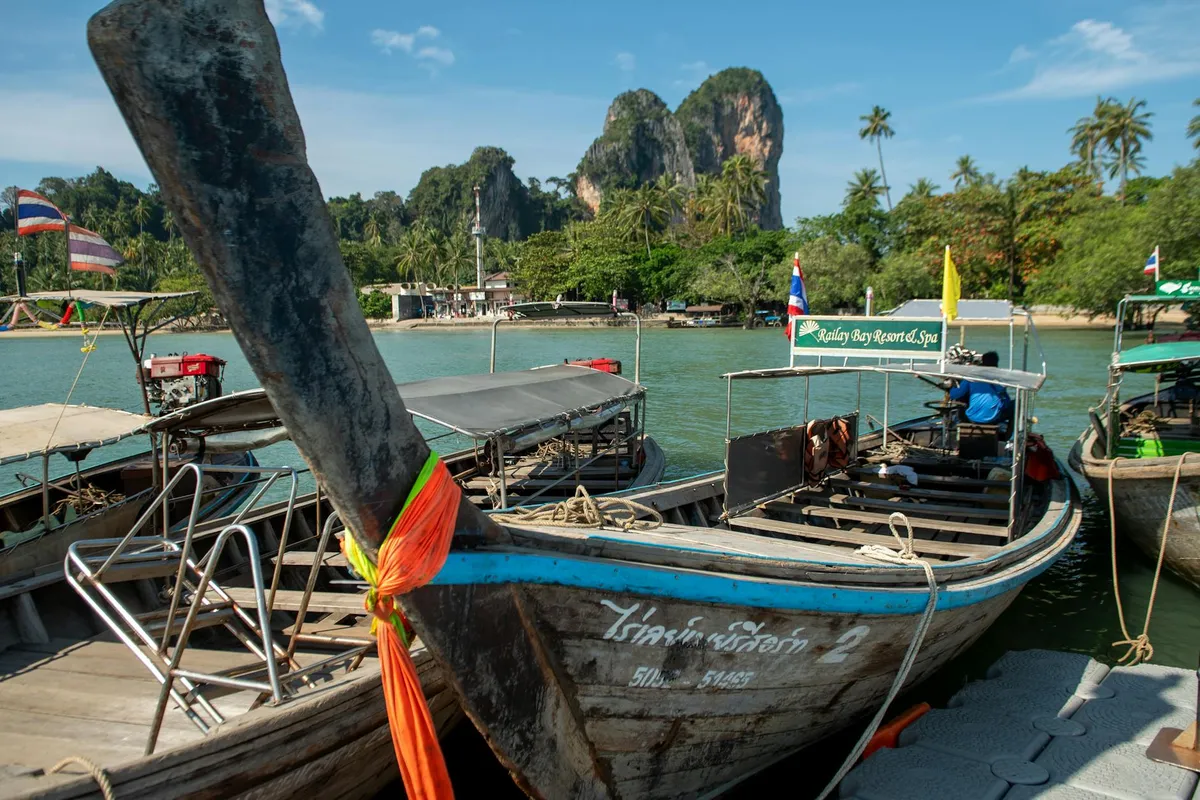 Long-tail boats anchored at Railay Beach in Krabi, Thailand, with limestone cliffs and lush greenery.