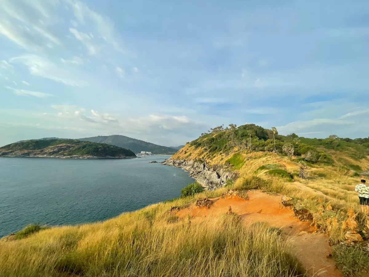 Explore the stunning coastal landscape of Promthep Cape, Phuket, with blue skies and rugged terrain.