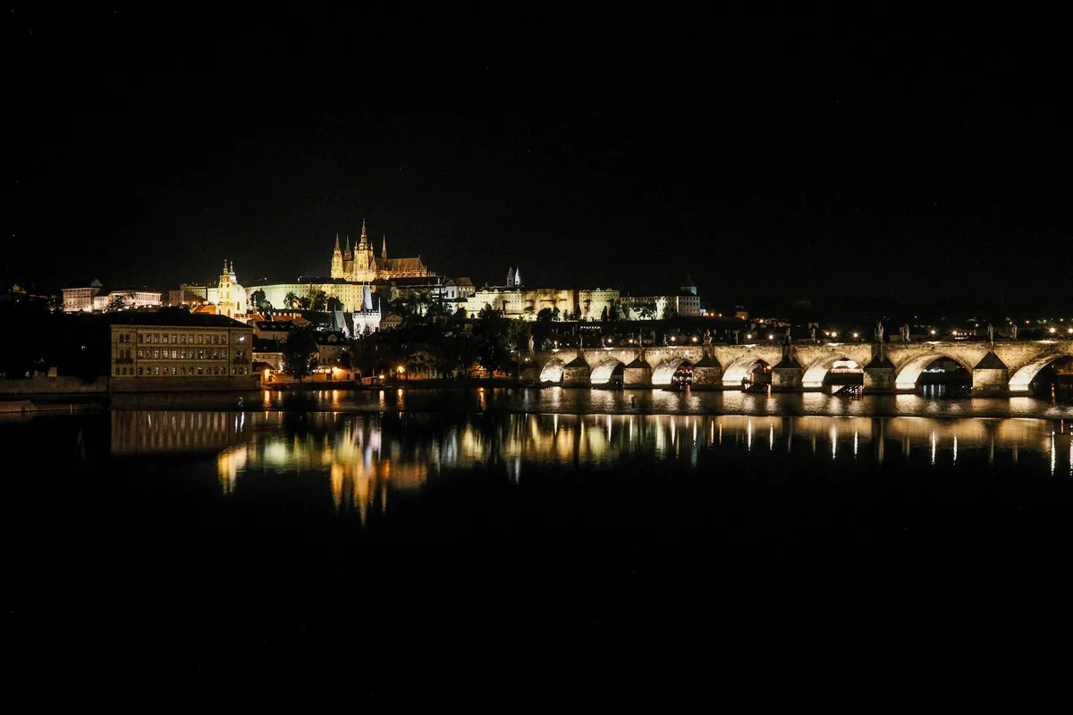 Stunning night view of Prague Castle and Charles Bridge reflecting on the Vltava River.
