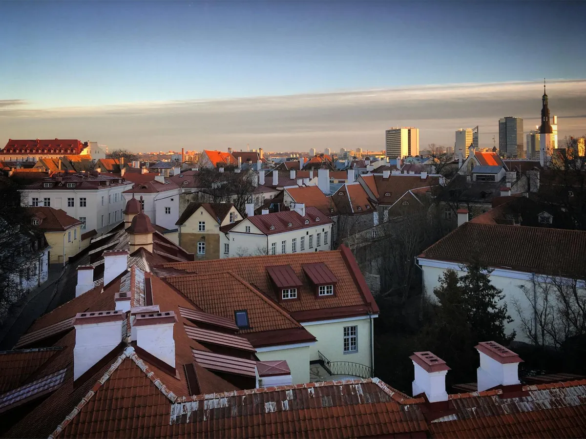 Stunning aerial view of Tallinn's Old Town with red rooftops and modern skyline at sunset.