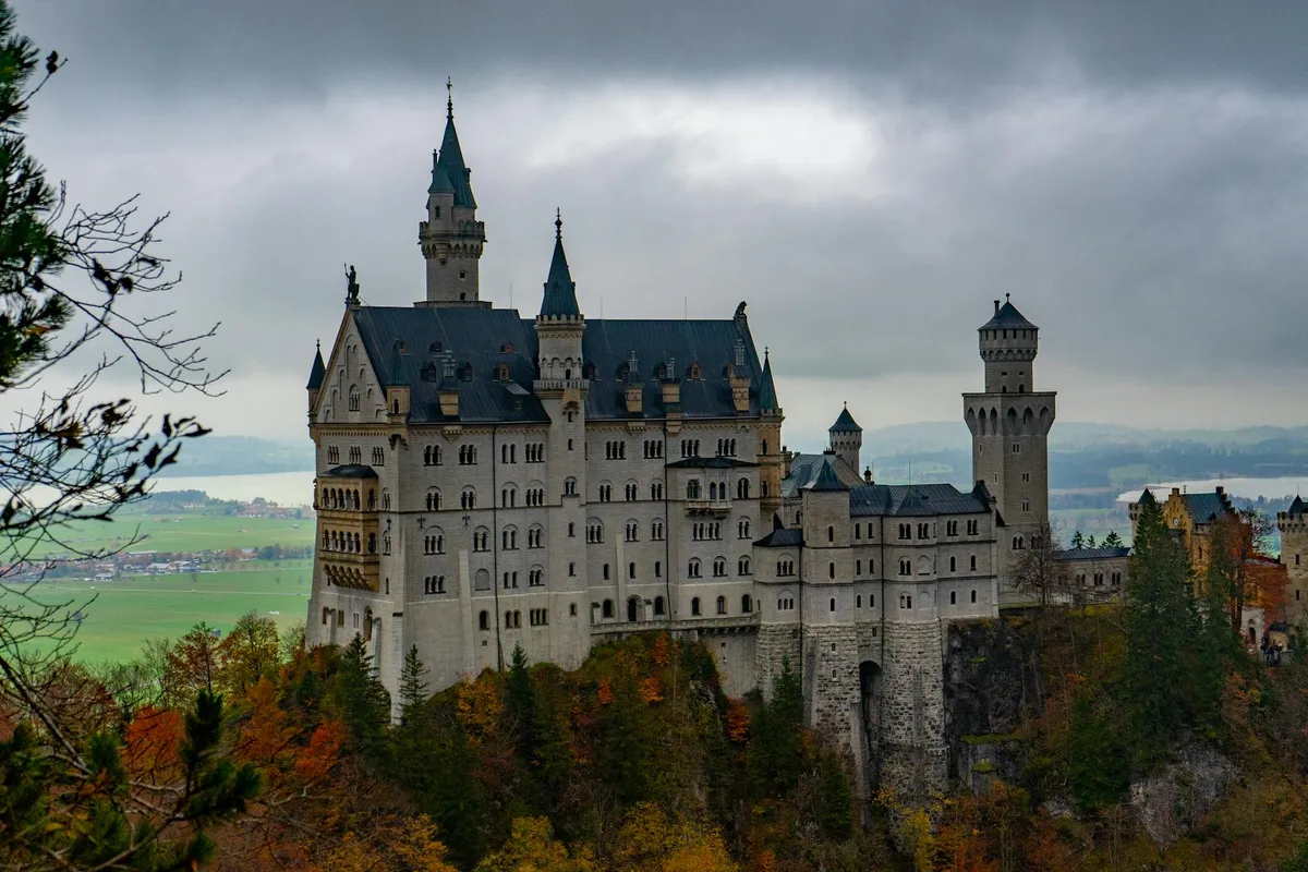 Dramatic view of Neuschwanstein Castle amidst colorful autumn foliage in Bavaria, Germany.