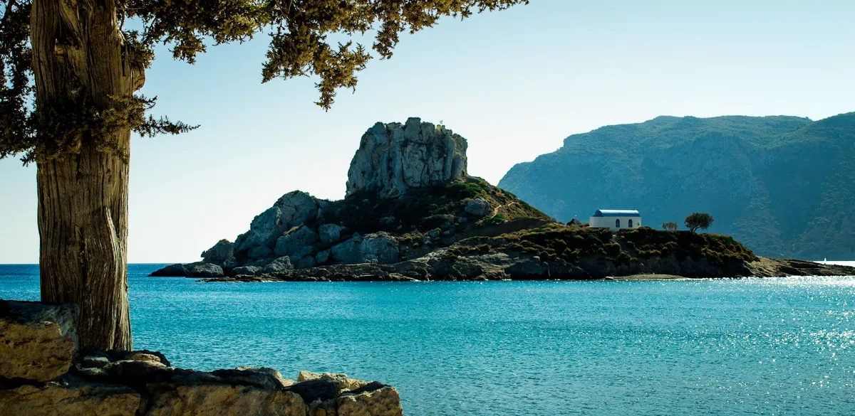 Beautiful coastal view of Kos, Greece featuring a rocky island and vibrant blue waters.