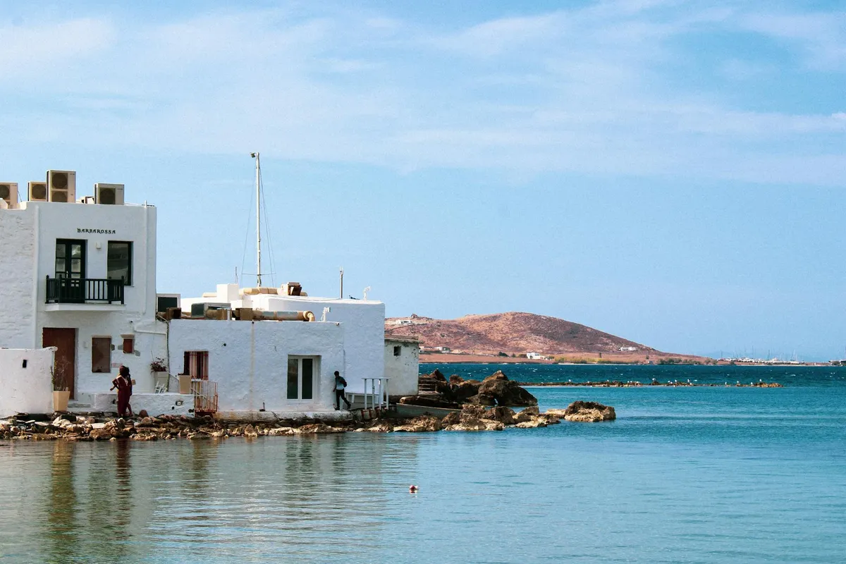 Charming white buildings by the coast in Naoussa, Paros Island with serene blue waters and hills in the background.