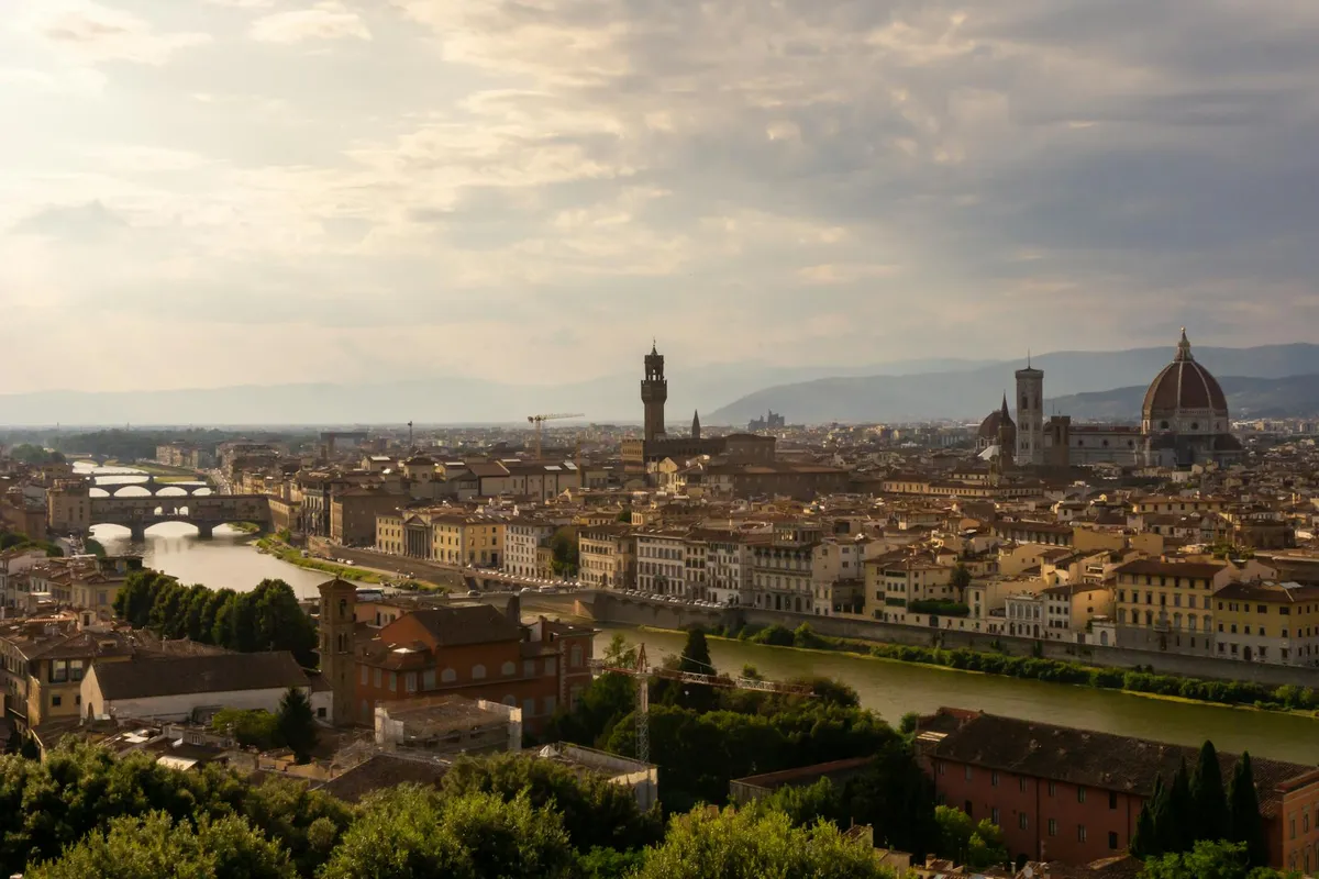 Panoramic view of Florence, Italy featuring the iconic Duomo and Arno River at sunset.