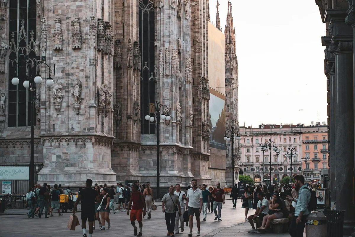 Captured at sunset, people gather at the iconic Piazza del Duomo in Milan, showcasing the stunning Duomo Cathedral.