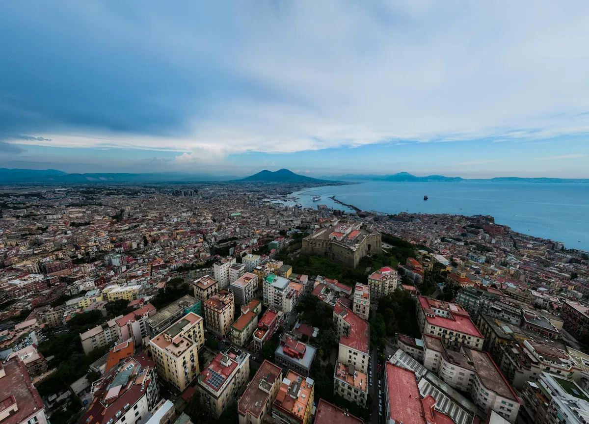 Panoramic aerial view of Naples, Italy, featuring Mount Vesuvius and the Mediterranean Sea.