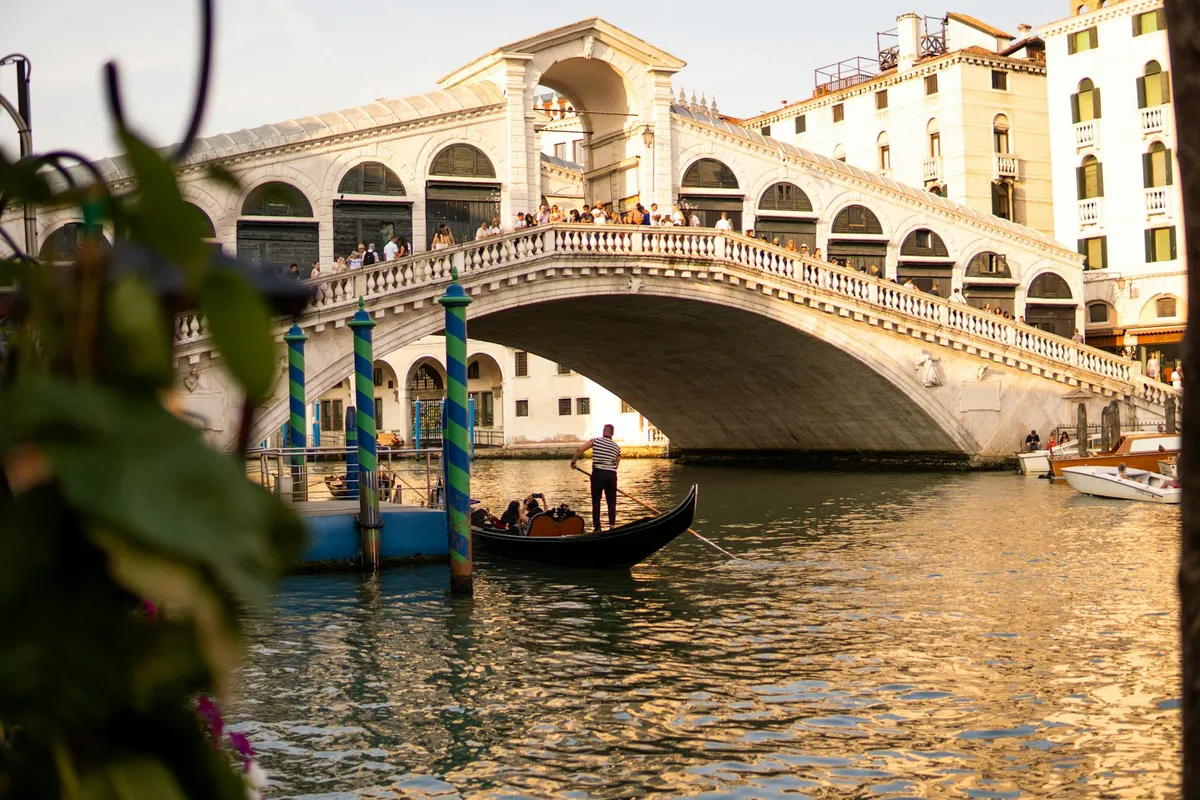 A gondola navigates the Grand Canal with Rialto Bridge lit by the setting sun in Venice, Italy.