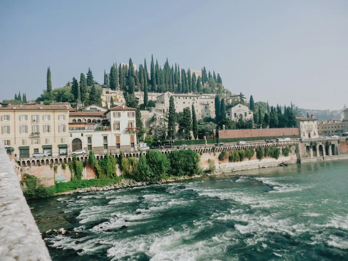 Beautiful photograph capturing Castel San Pietro in Verona, Italy with lush greenery and flowing river.