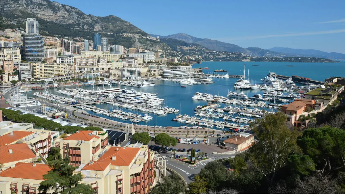 A stunning aerial view of Port Hercules with yachts in Monaco, framed by the cityscape and mountains.