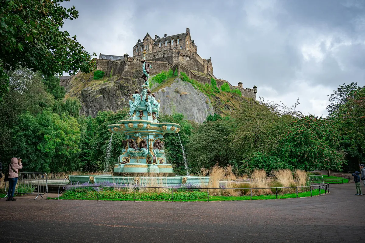 Beautiful view of Edinburgh Castle and Ross Fountain surrounded by lush greenery in Scotland.